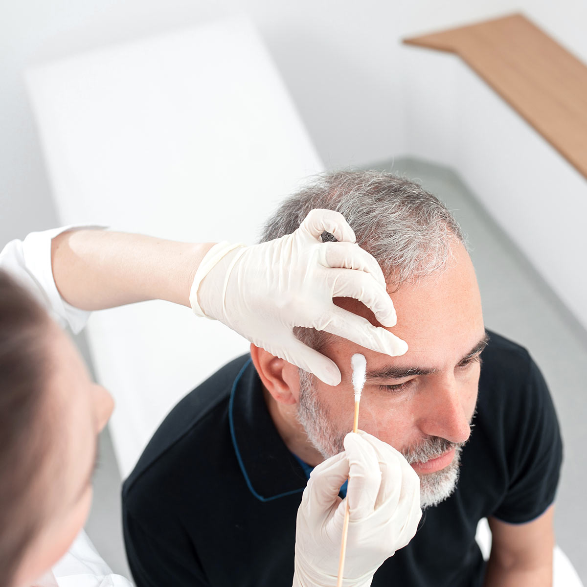 A middle aged mad seen from above while a nurse applies a skin cancer removal fluid to his forehead.