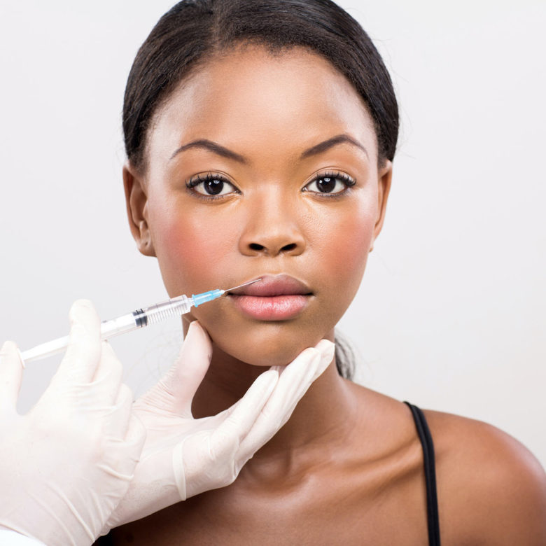 A young Black woman receives a cosmetic injection to her upper lip.