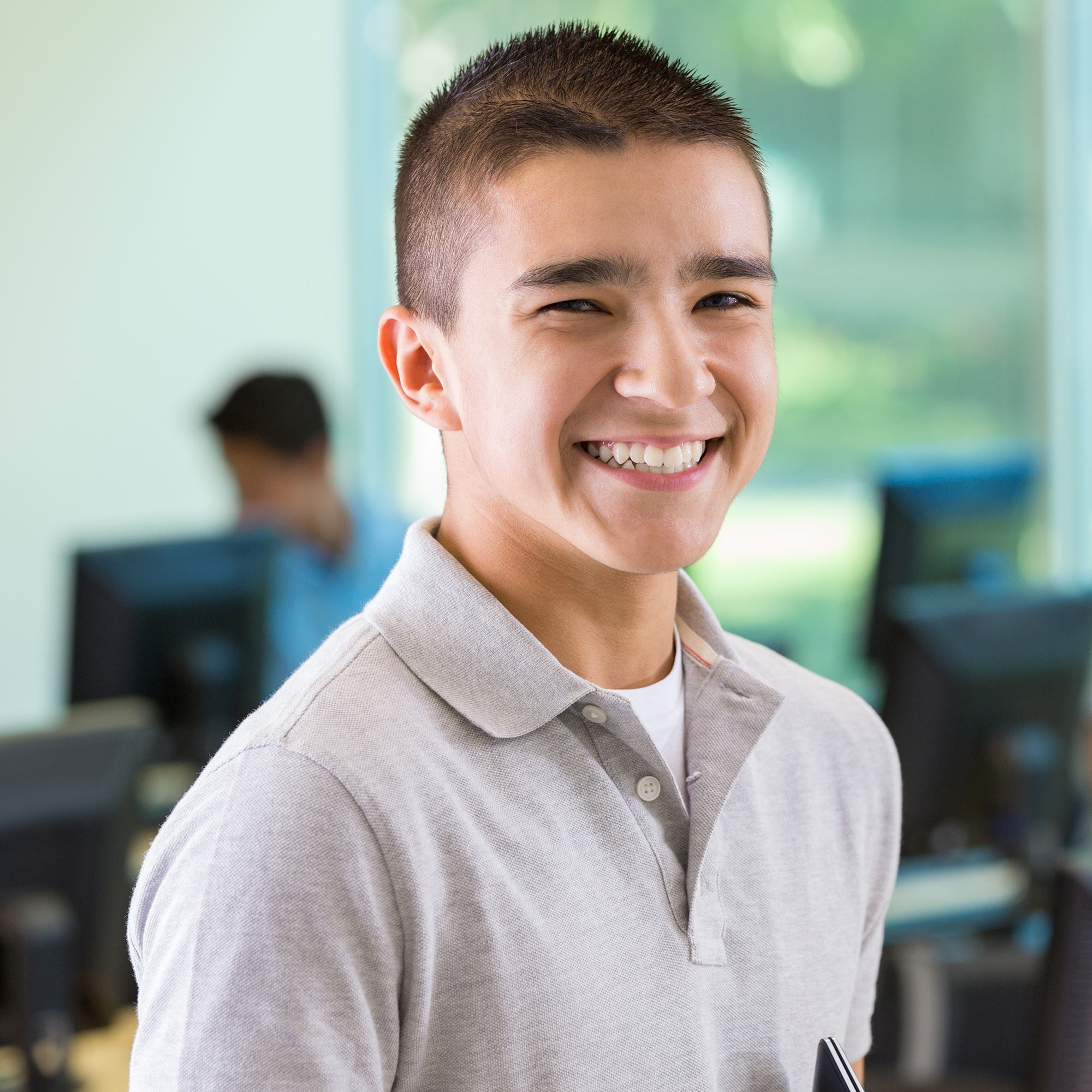 A teen boy in a gray polo shirt smiles confidently at the camera.