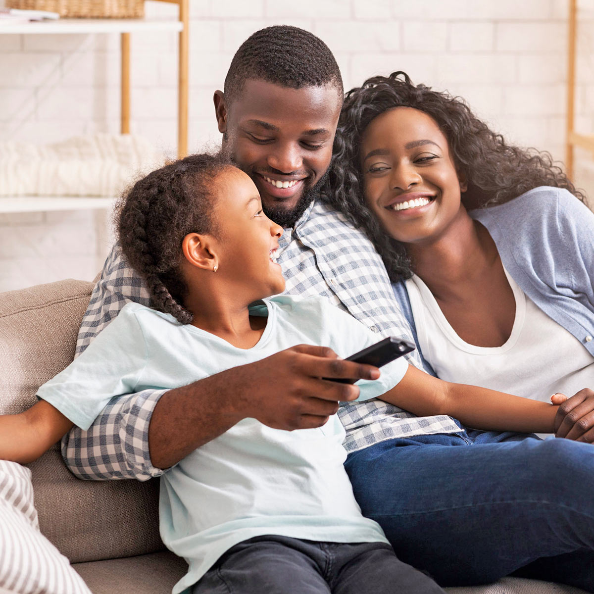 A young Black girl with her dad and mom shares a cuddles and laugh with them on their sofa.
