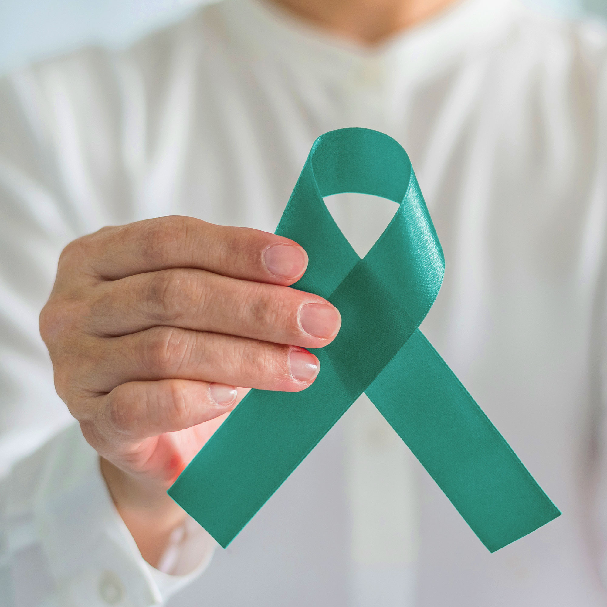 Closeup of a male doctor's hand holding the green ribbon that symbolizes scleroderma awareness month.